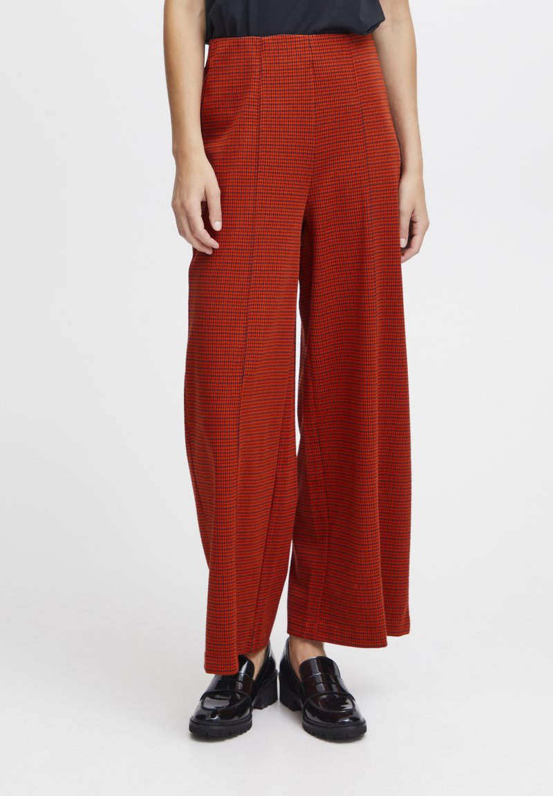 Pantalons à taille haute et jambes larges en motif vichy rouge et noir, présentant un tissu lisse et des plis subtils, accompagnés de mocassins noirs brillants.