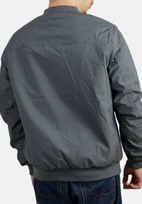 Chaqueta bomber gris con una textura suave, ribetes acanalados y dobladillo elástico. Diseño sencillo sin marcas ni patrones visibles.
