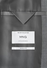 Inderside af habitjakke med gråt for, der viser mærkets label "MNG The Suit Collection" og "Regular Fit" størrelse EU 50 / UK-USA-MEX 40.