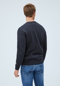 Námořnická modrá mikina s dlouhými rukávy, žebrovanými manžetami a lemem. Jednoduchý design, vyrobeno z bavlny, s malým logem na levém rukávu.