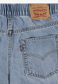 Jeans de denim azul claro con cinturilla elástica, que presentan costuras amarillas, un parche de cuero de la marca y un diseño clásico de bolsillo trasero.
