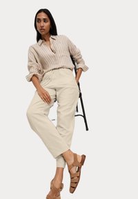 Randig beige knappad skjorta, krämfärgade avsmalnande byxor och bruna öppna sandaler. Texturerade tyger och avslappnad passform.