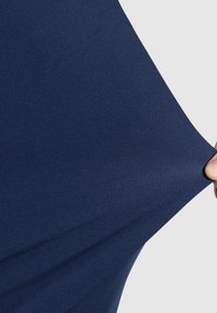 Marynarska tkanina elastyczna naciągnięta, podkreślająca gładką teksturę i elastyczność. Powierzchnia ma jednolity, delikatny wzór. Brak widocznego wykończenia.