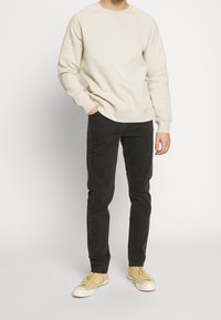 Beige bavlněná mikina, černé džínové kalhoty a žluté plátěné tenisky. Mikina má elastické manžety a design s kulatým výstřihem.