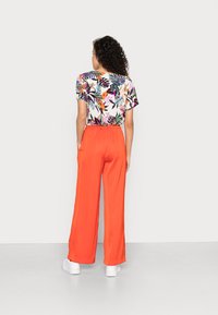T-shirt de manga curta com estampa floral em branco e folhas coloridas, emparelhado com calças largas de um vibrante laranja. Ténis brancos completam o visual.