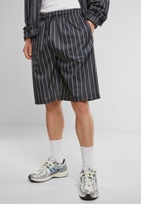 Shorts noirs à rayures avec une taille élastique, offrant un ajustement décontracté. Associés à des chaussettes blanches et des baskets argentées avec des accents bleus.
