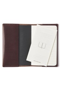 Donkerbruine leren notitieboekomslag met stiksels. Aan de binnenkant is een zwarte map en een wit gelinieerd notitieboek zichtbaar, met een Moleskine-label.