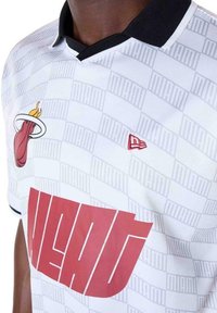 Witte korte mouwen jersey met een zwarte kraag, met een rode tekst "HEAT" en een Miami Heat-logo. Achtergrondpatroon bevat subtiele tekst "MIAMI".