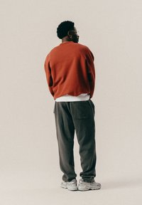 Rød oversized sweatshirt, hvid lagdelt skjorte underneden, mørkegrå posede bukser og grå sneakers, set fra bagen.