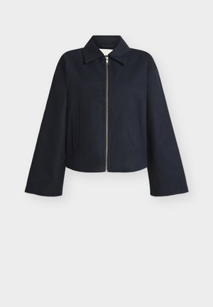 Črna bunda z zadrgo, širokimi rokavi, ovratnikom in dvema stranskima žepoma na enobarvni svetli podlagi.