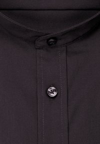 Gros plan d'un col de chemise noir avec un col mandarin et deux boutons noirs visibles sur la patte de boutonnage.