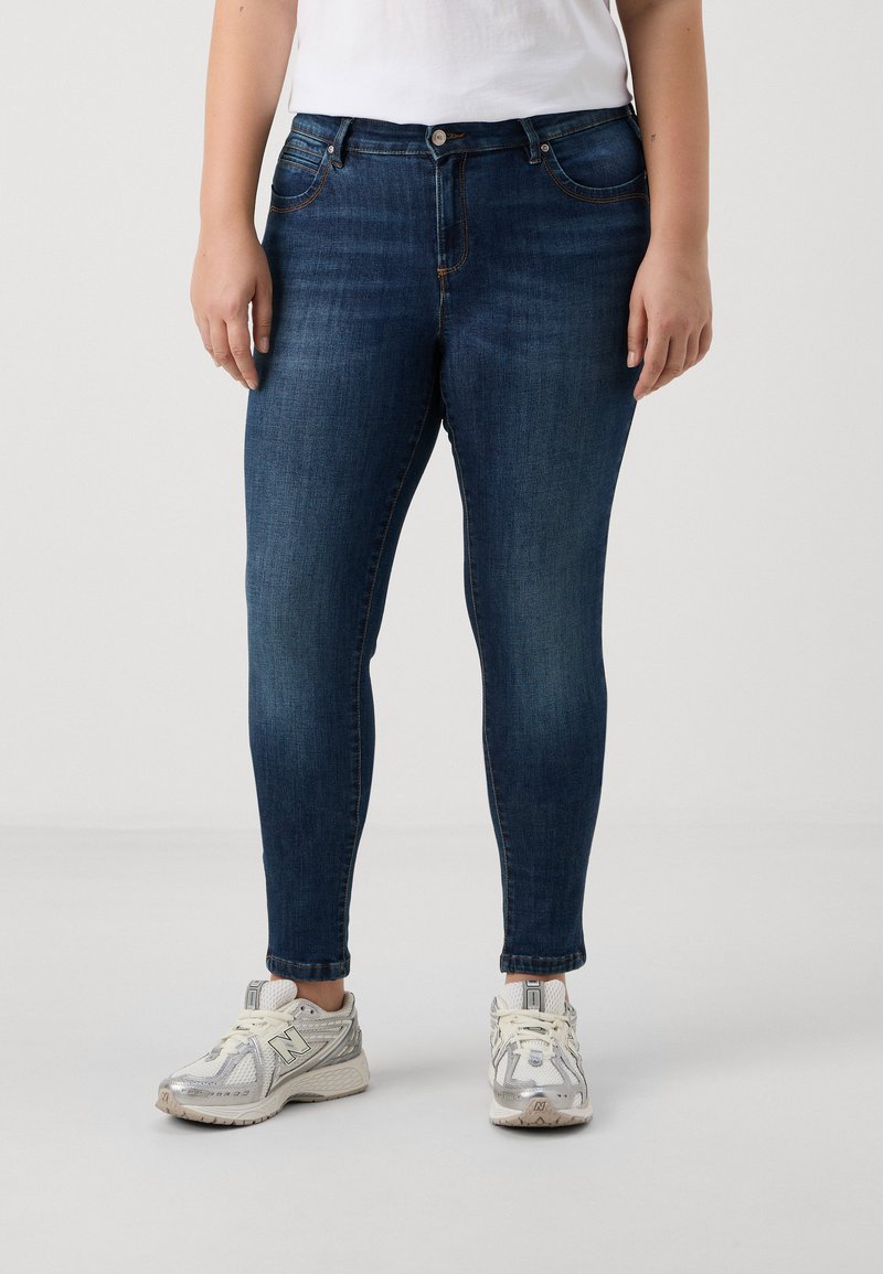 Skinny blue jeans made of denim with subtle fading, five-pocket design, front button closure, paired with gray and white sneakers.