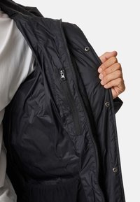 Black jacket interior featuring a smooth, shiny material. Includes zipper and snap fasteners. Partial view of white shirt underneath.