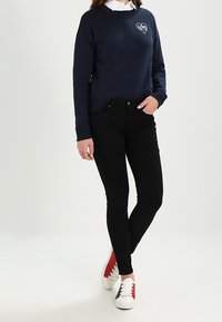Sudadera de color marino con un gráfico de un corazón que dice "LOVE", combinada con jeans skinny negros y zapatillas blancas con detalles en rojo y azul.