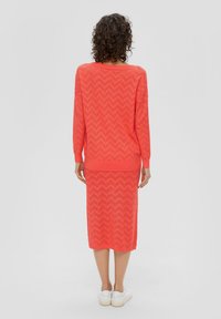 Coralowy sweter dzianinowy i zestaw spódnicy midi z wzorem w zygzak, długimi rękawami i prążkowanymi mankietami. Noszony z białymi sneakerami.