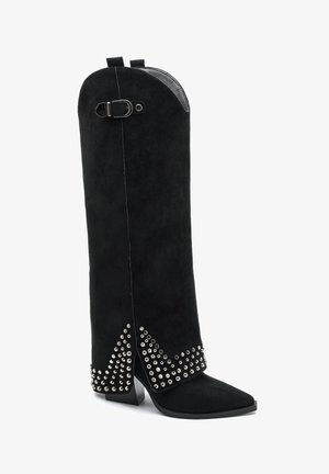 Botte noire en daim montant jusqu'au genou, avec bout pointu, talon carré, clous argentés en motif zigzag, et une boucle décorative près du haut.
