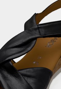 Gros plan d'une lanière de sandale en cuir noir torsadée sur une semelle beige avec texte visible indiquant la taille et la marque à l'intérieur.