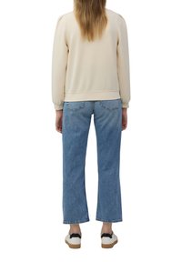 Felpa beige con una vestibilità rilassata e maniche a sbuffo, abbinata a jeans a gamba larga blu chiaro e sneakers bianche con dettagli neri.