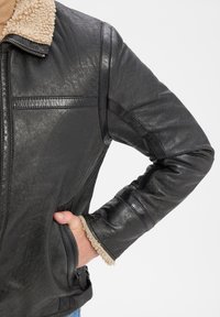 Schwarze Lederjacke mit einem beigen Lammfellkragen, seitlichem Reißverschlusstasche und strukturiertem Finish. Der Ärmel verfügt über eine horizontale Nahtdetails.