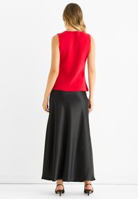 Red sleeveless top paired with a black satin maxi skirt. The top features a smooth texture and a tailored fit.