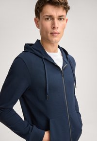 Marineblauer Zip-Hoodie aus weichem Stoff. Verfügt über eine Kapuze mit Kordelzug, Fronttaschen und eine glatte Textur. Sichtbares Reißverschluss-Detail.