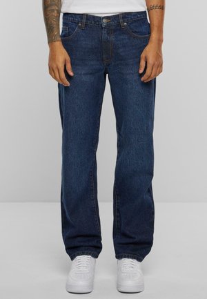 Mørkeblå, rette jeans med fem lommer, sydd detaljer og messingknap lukning, iført hvide sneakers.