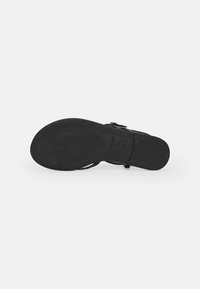 Black sandal sole with textured rubber for grip, featuring a flat design and a smooth finish. Straps are minimalist with adjustable buckle.