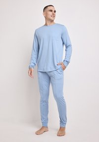 Lysblå langærmet top med en brystlomme, parret med matchende tapered bukser. Blødt stof med en glat tekstur, minimalistisk design.