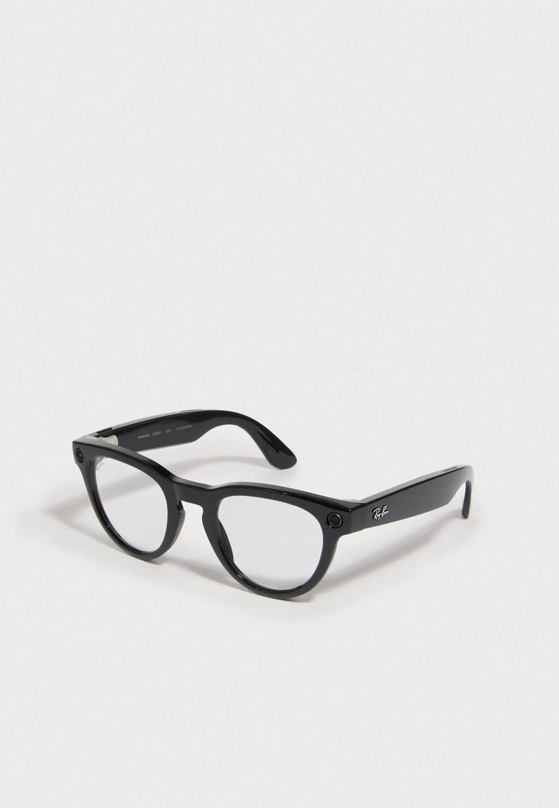 Occhiali neri in plastica con lenti trasparenti, forma arrotondata e dettagli metallici sui lati. Presentano un logo sulla tempia.