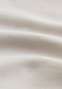 Tejido ribeteado en color beige claro con una textura suave, que presenta finas líneas verticales y un ligero estiramiento para mayor flexibilidad.