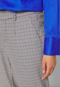 Blouse en satin bleu à manches longues associée à un pantalon à carreaux houndstooth marron et blanc avec des accents bleus, mettant en avant une texture lisse.