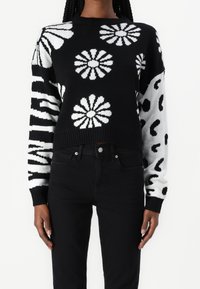 Black and white knitted sweater featuring large floral patterns, stripes, and a cropped design with ribbed cuffs and hem.