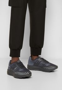 Chaussures de sport présentant un dégradé de bleu foncé à bleu clair, une tige en mesh texturé et une semelle noire contrastante avec des motifs d'adhérence.