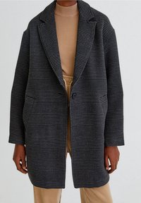 Cappotto a plaid grigio con rever a punta, chiusura a un bottone e due tasche laterali. Tessuto intrecciato con strisce scure e chiare alternate.