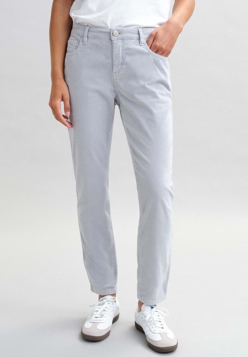 Světlé šedé kalhoty s rovný fit, s předními kapsami, zapínáním na knoflík a hladkým povrchem. Nosené s bílými sportovními botami.