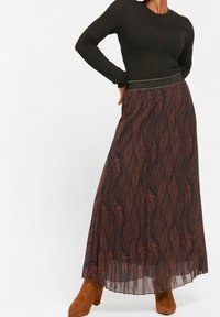 Lång blommig kjol med svart bas och bruna bladmönster, kompletterad med en åtsittande svart ribbad topp och detaljer i metall på midjan.