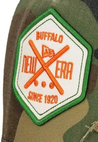 Die grüne Camouflage-Cap verfügt über ein gesticktes Patch in hexagonaler Form. Das Patch zeigt "BUFFALO" und "NEW ERA" in Orange, mit gekreuzten Schlägern und Punkten.