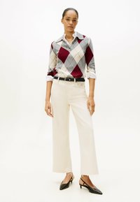 Maglione argyle grigio, rosso e crema con maniche lunghe, abbinato a pantaloni a gamba larga crema e décolleté nere a punta.