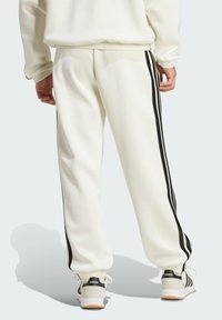 Bijele atletske hlače s crnim bočnim trakama, elastičnom trakom oko struka i rebrastim manžetama. Upotpunjene bijelim i crnim tenisicama s logom.