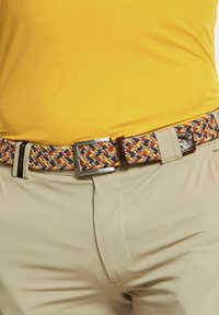 Gewebter mehrfarbiger Gürtel mit gelben, roten und blauen Mustern, mit einer silbernen Metallschnalle und braunen Lederakzenten. Getragen mit beigen Hosen.