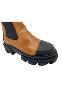 Bota de tornozelo em couro castanho com biqueira e sola em borracha preta. Apresenta painéis laterais elásticos e uma sola exterior rugged e texturizada para maior tração.