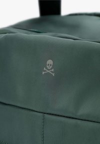 Grüner Stoffrucksack mit strukturierter Oberfläche, auf der Seite mit einem grauen Skull-und-Kreuzbone-Emblem bedruckt.
