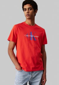 Camiseta de algodón roja con un logo azul "CK" y el texto "Calvin Klein Jeans". Con mangas cortas y un clásico cuello redondo.