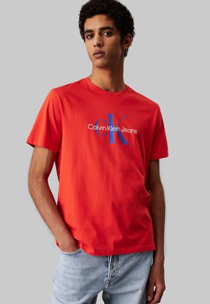 Rød bomulds T-shirt med et blåt "CK" logo og teksten "Calvin Klein Jeans". Korte ærmer og en klassisk rund hals.
