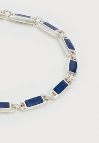 Ezüst lánc karkötő, amelyen téglalap alakú sötétkék zománc betétek vannak, ovális ezüst gyűrűk által összekapcsolva, fehér háttér előtt.