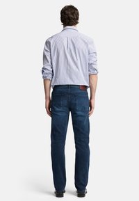 Camicia a righe blu chiaro con maniche arrotolate, abbinata a jeans blu scuro con un'etichetta di pelle sul retro e dettagli di cucitura sottili.
