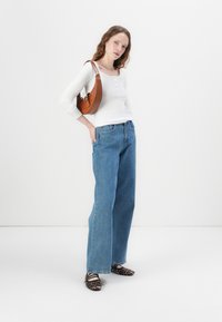 Hvit langermet henley skjorte, blå vide jeans, brun veske med krokodilleprøvning, og leopardskinnsko. Enkel hvit bakgrunn.