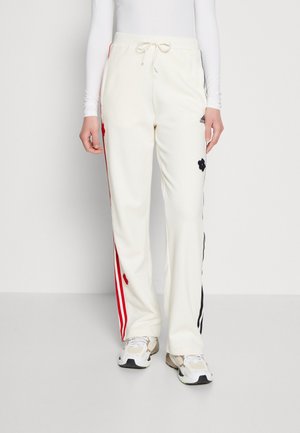 Białe spodnie dresowe z czerwono-czarnymi paskami po bokach, kwiatowe naszywki, logo Adidas, noszone z białymi trampkami i białą bluzką z długim rękawem.