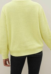 Hellgelber, gestrickter Pullover mit lockerem Sitz, gerippten Bündchen und rundem Ausschnitt. Die strukturierte Stoffoberfläche zeigt eine offene Webstruktur.