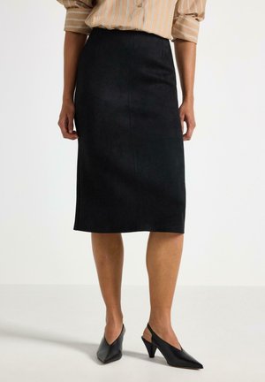 Kvinde iført en sort knælængde blyantsnederdel, sorte slingback hæle med spids tå og en langærmet beige stribet skjorte med opkrogede ærmer.